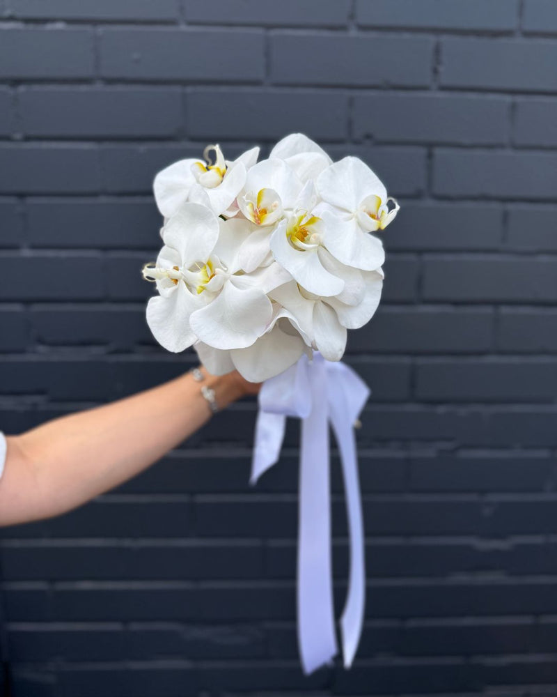 Delicate white orchid bouquet for bride with white ribbon accent.