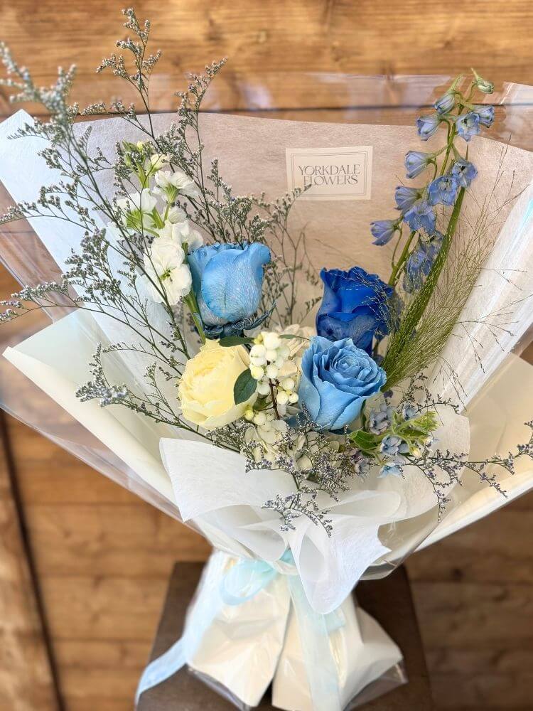 Bouquet of deep and light blue roses with greenery and white accents, wrapped in blue and white paper – elegant floral arrangement