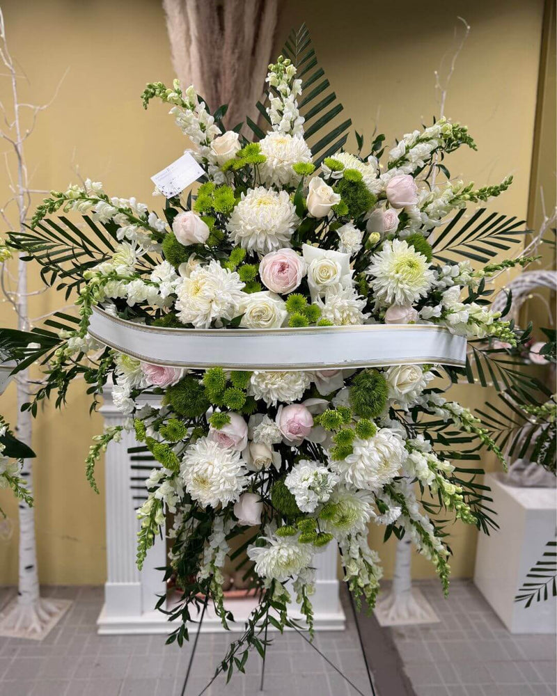 A standing floral arrangement in white, pink and green shades, for sympathy or funeral purposes.