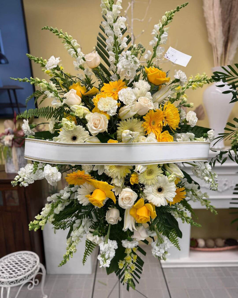 Standing sympathy flower spray in yellow and white for funeral services.