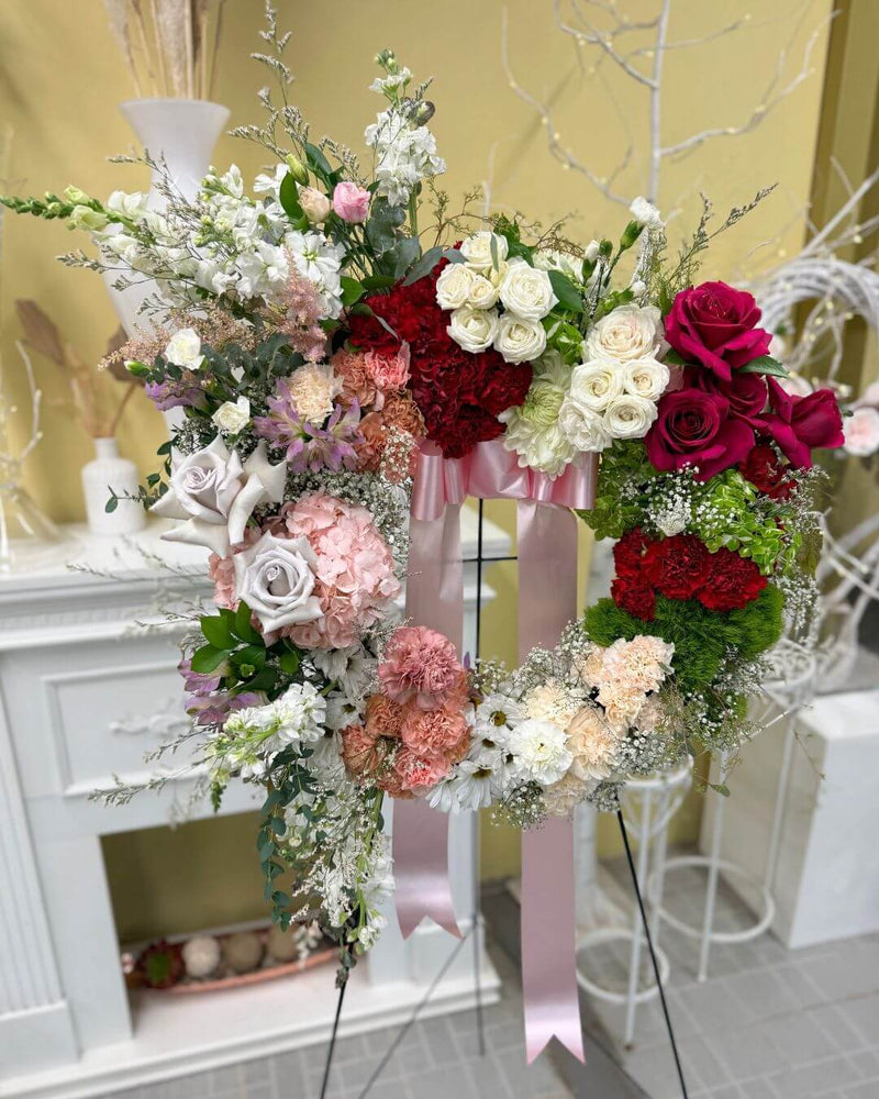 Floral sympathy wreath featuring roses in a fading red to blush palette with greenery.