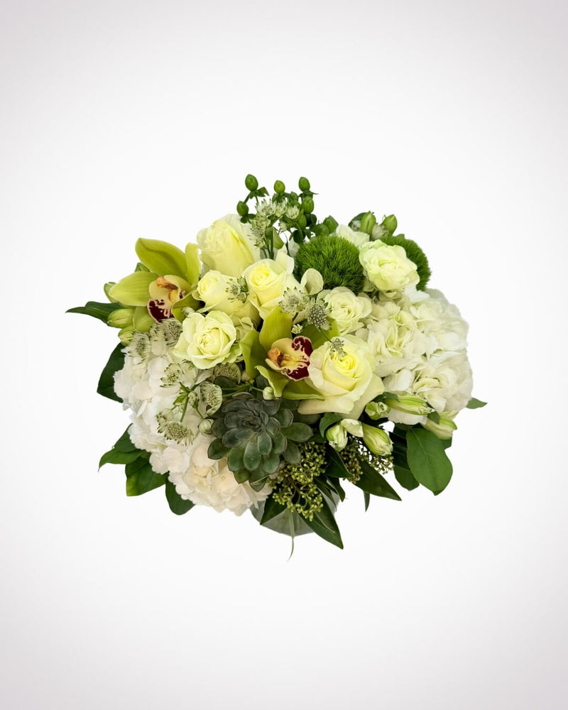 A vase arrangement of white hydrangea, roses, orchids, and green foliage.