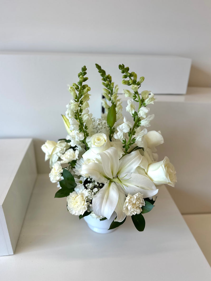 Centrepiece with crisp white blooms balanced with lush greenery in a white vase.
