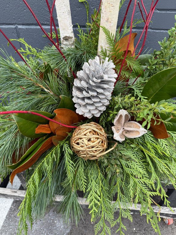 Decorative winter planter arrangement of greenery, pinecones, and branches.
