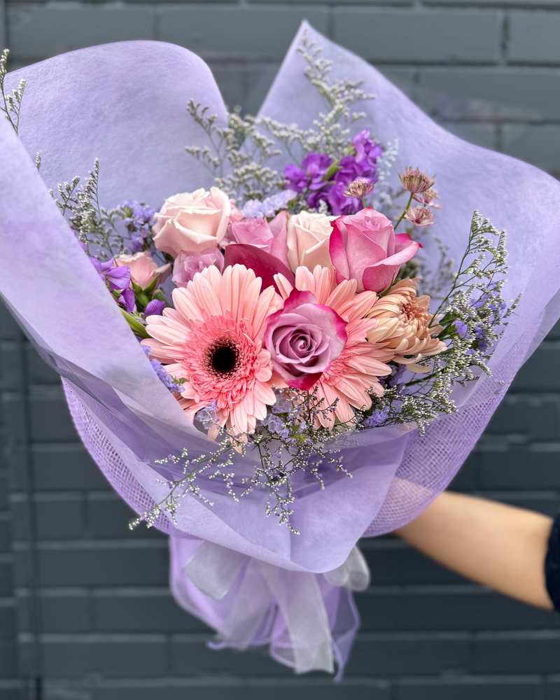 Bouquet of pink and lavender flowers wrapped in purple paper.