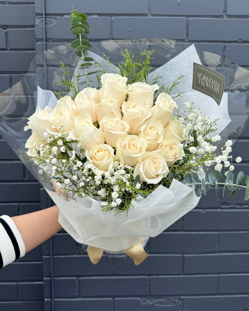 Bouquet of white roses with greenery in a white elegant wrapping.