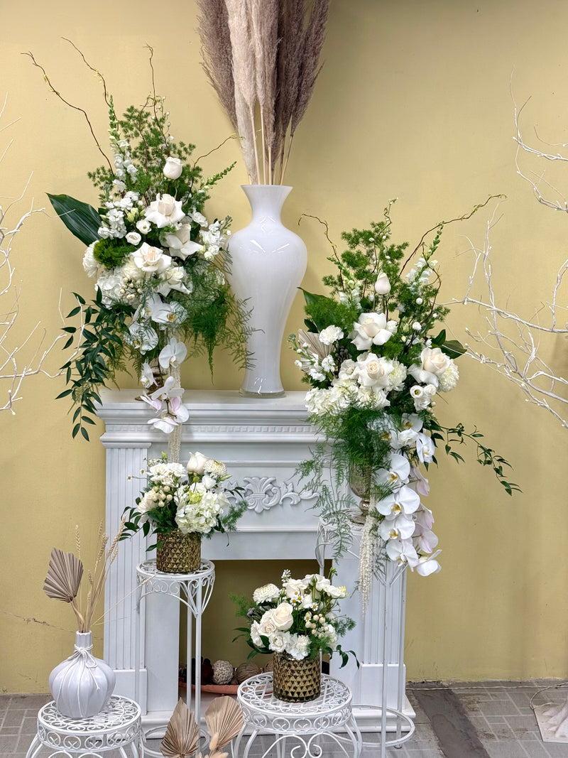 Set of tall elegant floral arrangement of white orchids and withe roses with lush greenery. 