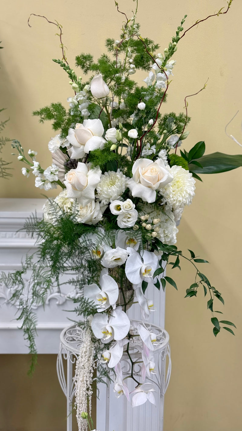 Tall elegant floral arrangement of white orchids and withe roses with lush greenery. 