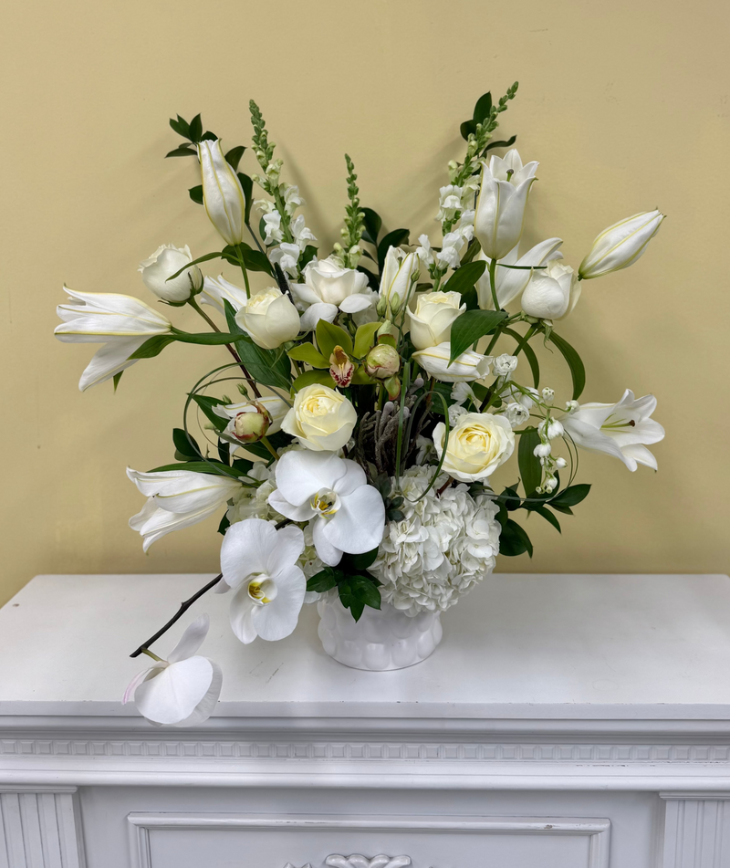 White and green arrangement with lilies and orchids in a withe vase.