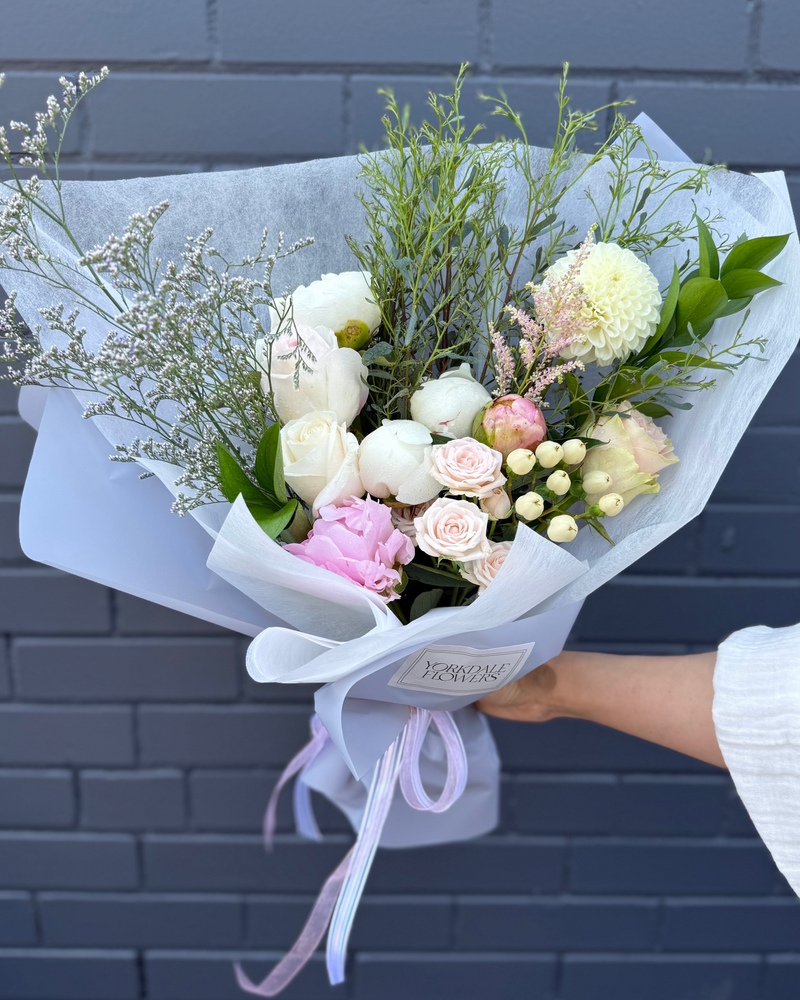 Mixed peony and dahlia bouquet, complete with rustic, natural greens wrapped in a light blue paper.