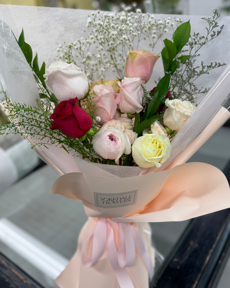 Red roses mixed with soft blush and white blooms bouquet. Wrapped in a peach color paper.