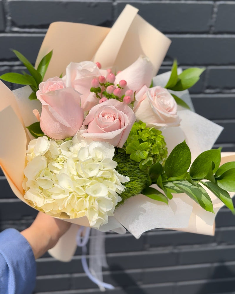 Bouquet of pink and white flowers with greenery wrapped in a light peach paper.