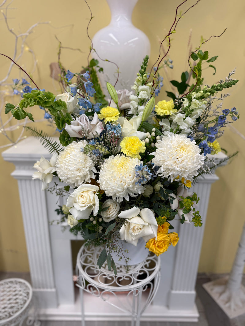 Florar arrangement with mix of white, blue, and yellow blooms .