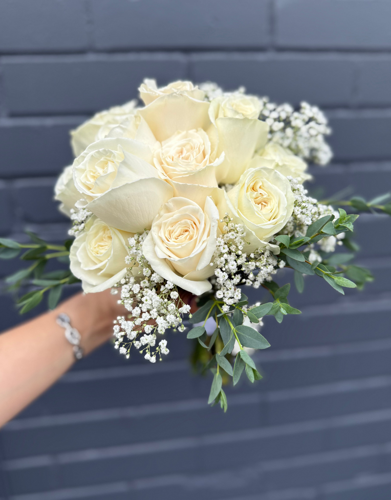 Classic bridal bouquet with fresh white roses, elegant greenery, and baby’s breath surrounded.