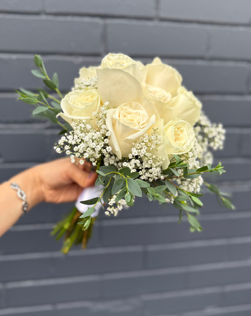 Classic bridal bouquet with fresh white roses, elegant greenery, and baby’s breath surrounded.