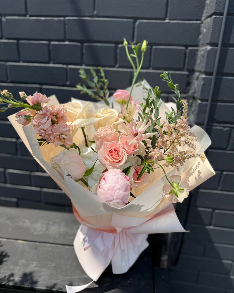 Bouquet of soft cream blooms with pale pink accents wrapped in soft cream paper.