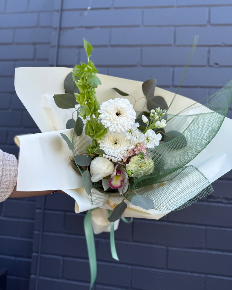 Minimal white floral bouquet with vibrant greenery wrapped in creamy paper and green netting.