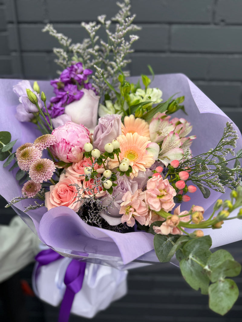 Mixed bouquet of flowers lavender and peach wrapped in purple paper.