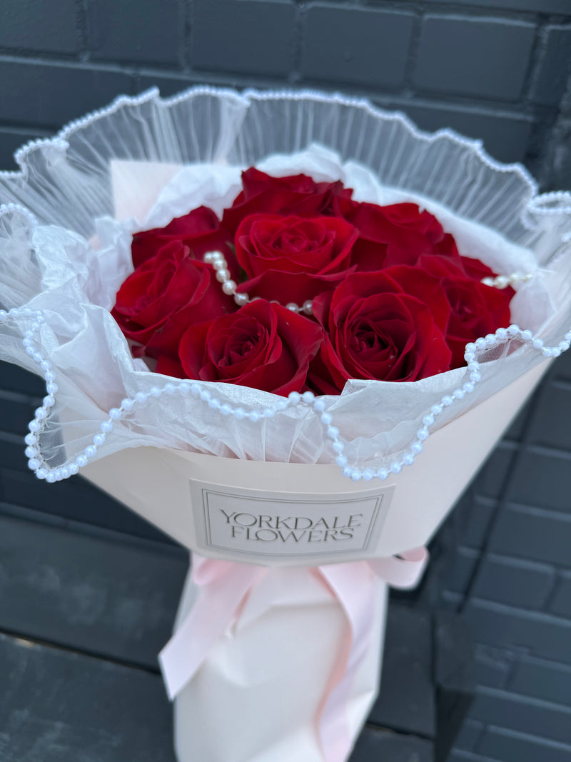 Bouquet of red roses with subtle hand-placed pearl accents around the wrapping.