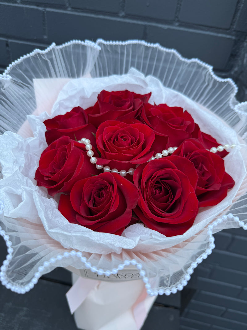 Bouquet of red roses with subtle hand-placed pearl accents around the wrapping.