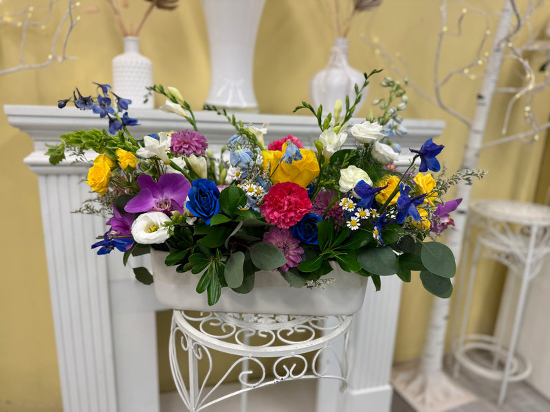 Colourful centrepiece arrangement mix of vibrant blooms in a rectangular white container. 