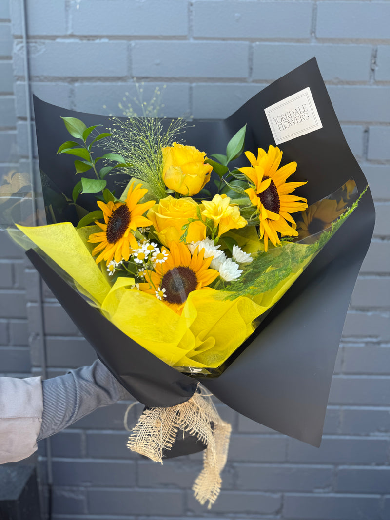 Cheerful arrangement of yellow sunflowers with textured blooms wrapped in a black paper.