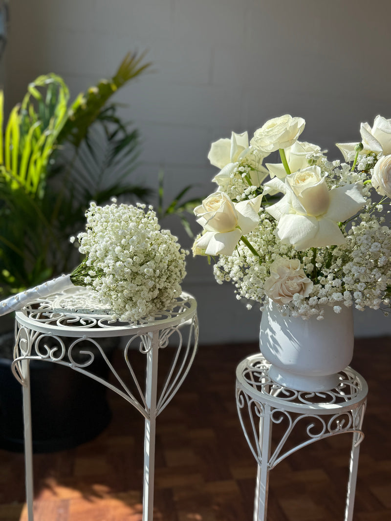 Bridal bouquet of delicate white baby’s breath next to a centrepiece with white roses and baby's breath.