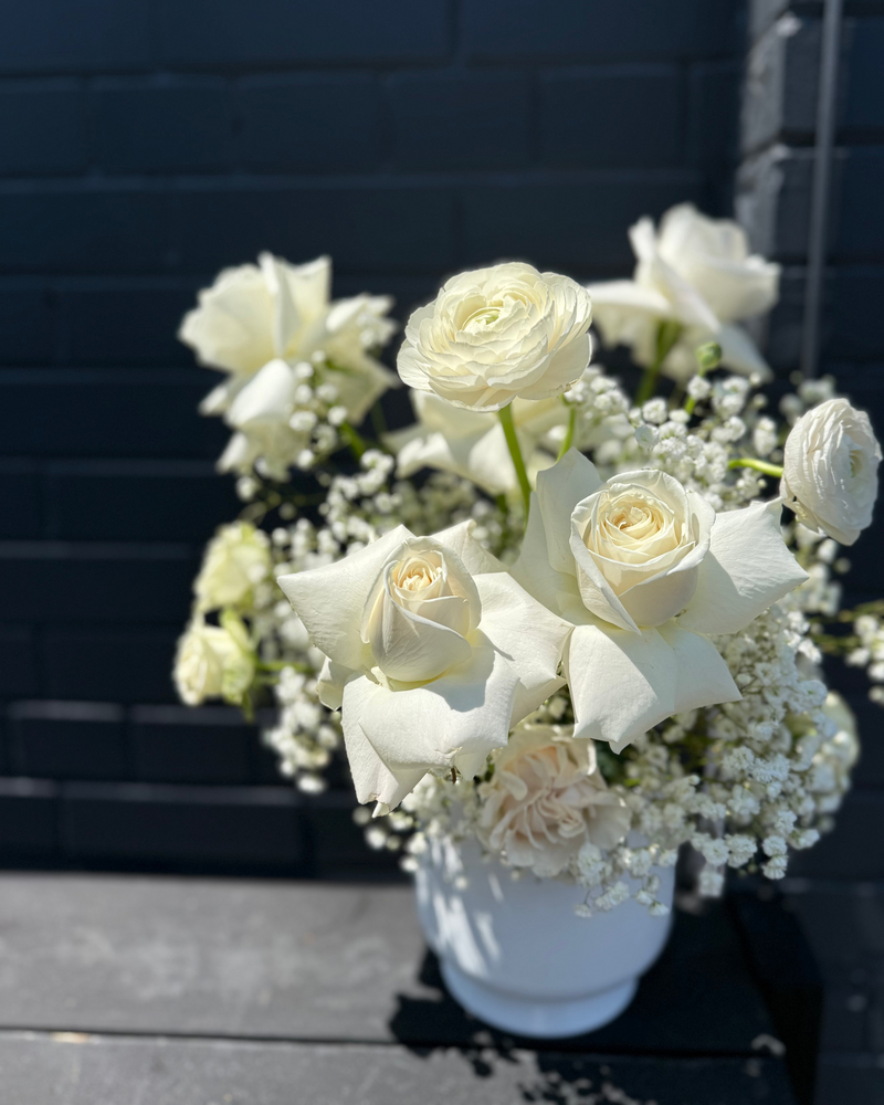 White floral centrepiece with pure white blooms and baby’s breath in a white cylinder vase.