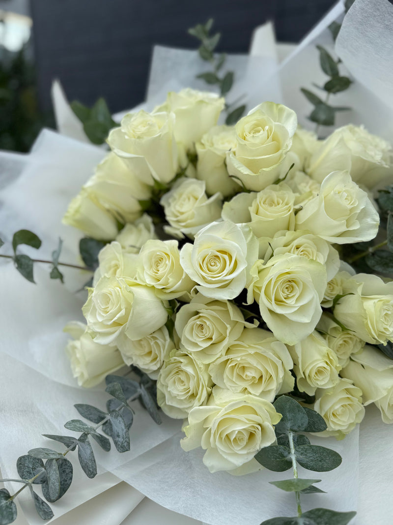 Fresh bouquet of fifty white roses with fragrant eucalyptus wrapped in white paper.