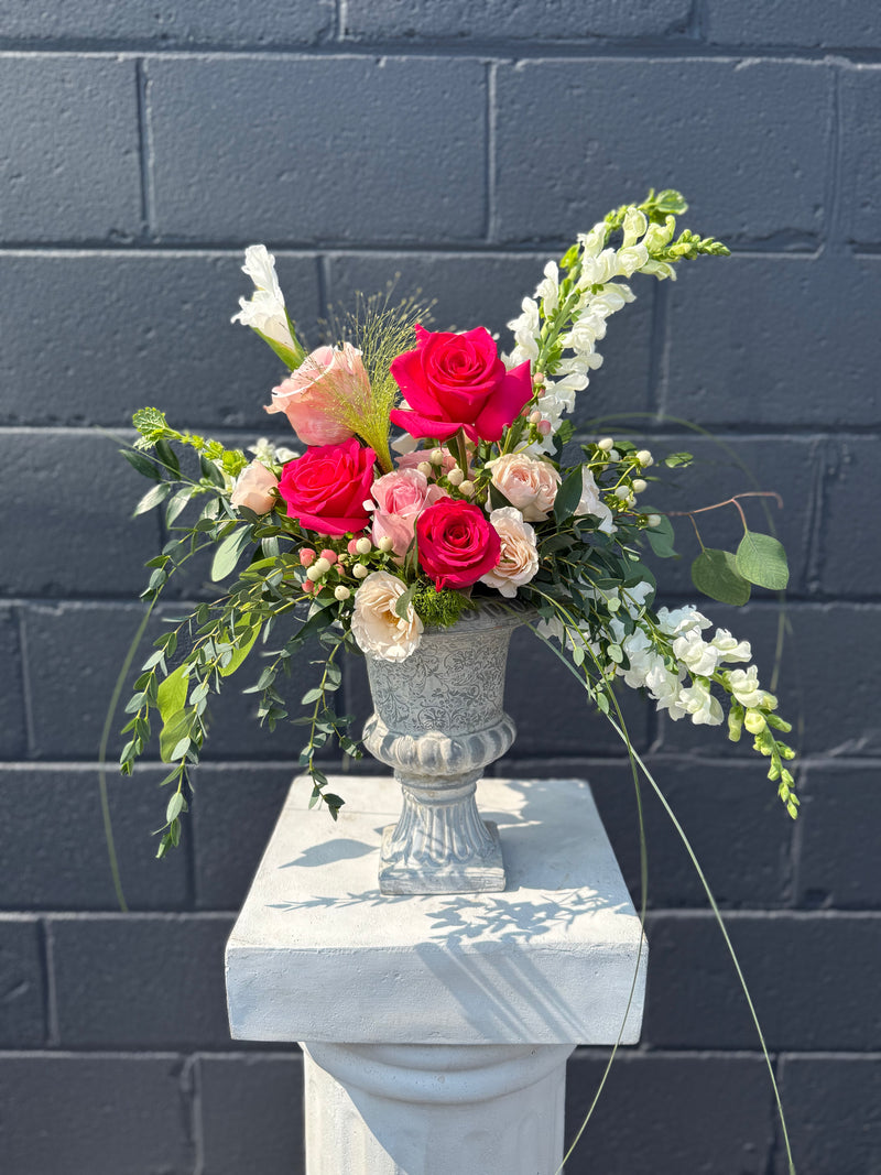 Bold hot pink blooms with peach and white accents arranged in a vintage vase centrepiece.
