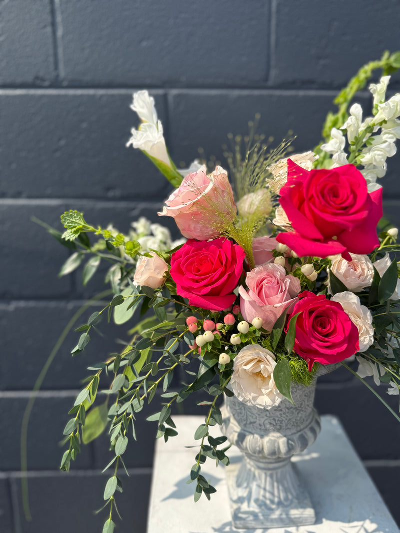 Bold hot pink blooms with peach and white accents arranged in a vintage vase centrepiece.