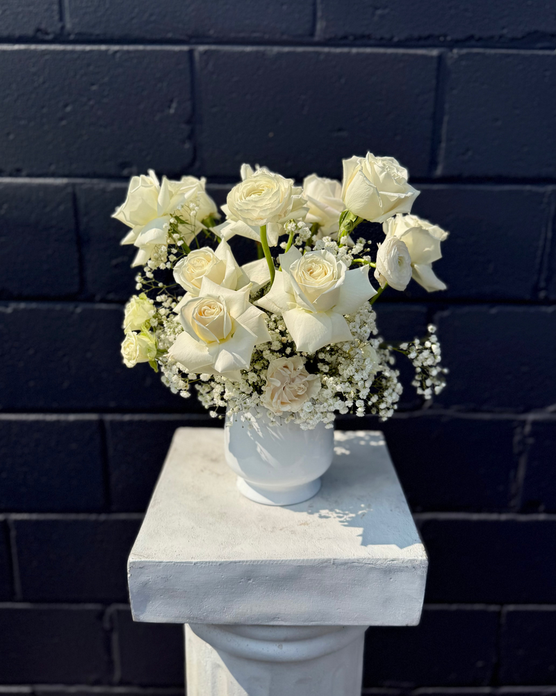 White floral centrepiece with pure white blooms and baby’s breath in a white cylinder vase.
