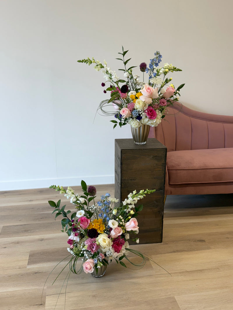 Set of two soft floral arrangement in blush and white with bursts of hot pink, yellow, and blue, displayed in a light brown vase – colorful centerpiece or gift bouquet