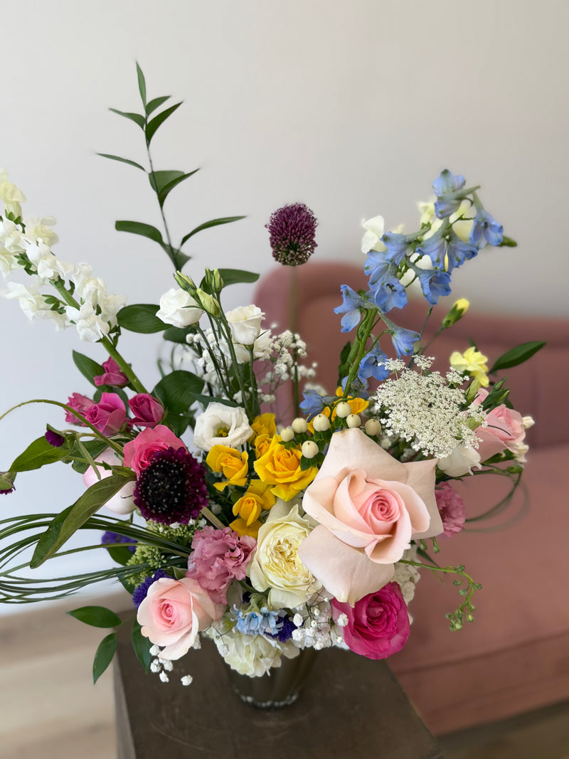 Soft floral arrangement in blush and white with bursts of hot pink, yellow, and blue, displayed in a light brown vase – colourful centrepiece or gift bouquet.