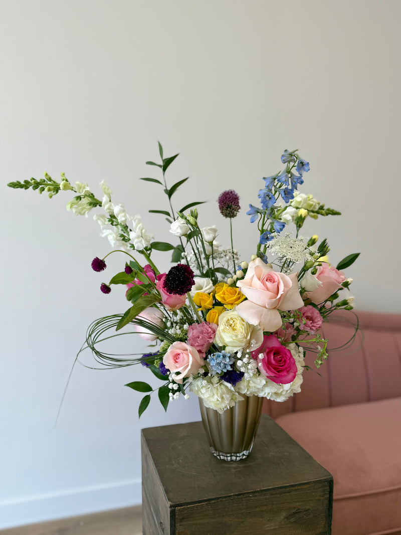 Soft floral arrangement in blush and white with bursts of hot pink, yellow, and blue, displayed in a light brown vase – colourful centrepiece or gift bouquet.