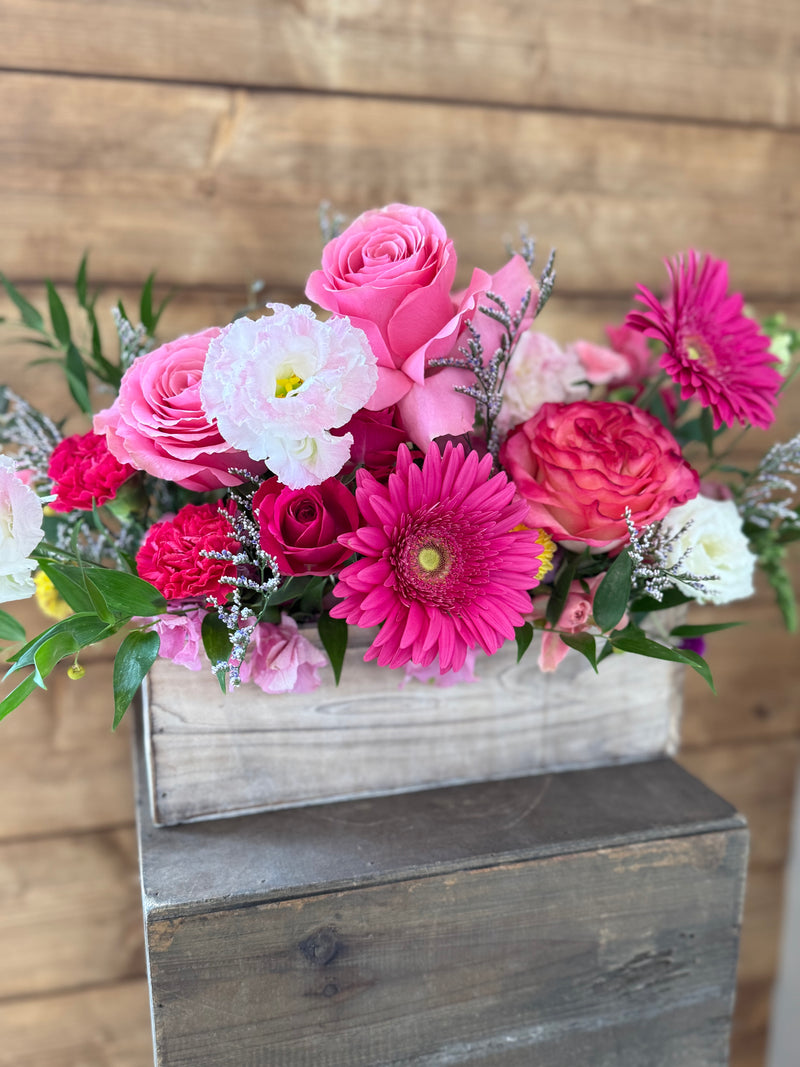 Bouquet of deep pink, red, and white flowers in a wooden container.