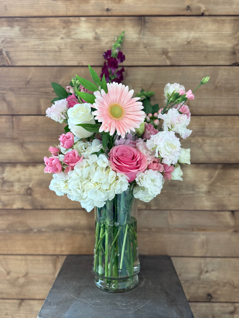Mixed pink and white floral arrangement displayed in a clear glass vase.