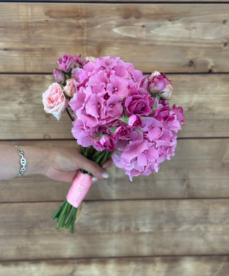 Bridal bouquet shaped with pink hydrangeas and mini roses, delicately tied with a pink ribbon – wedding floral arrangement.