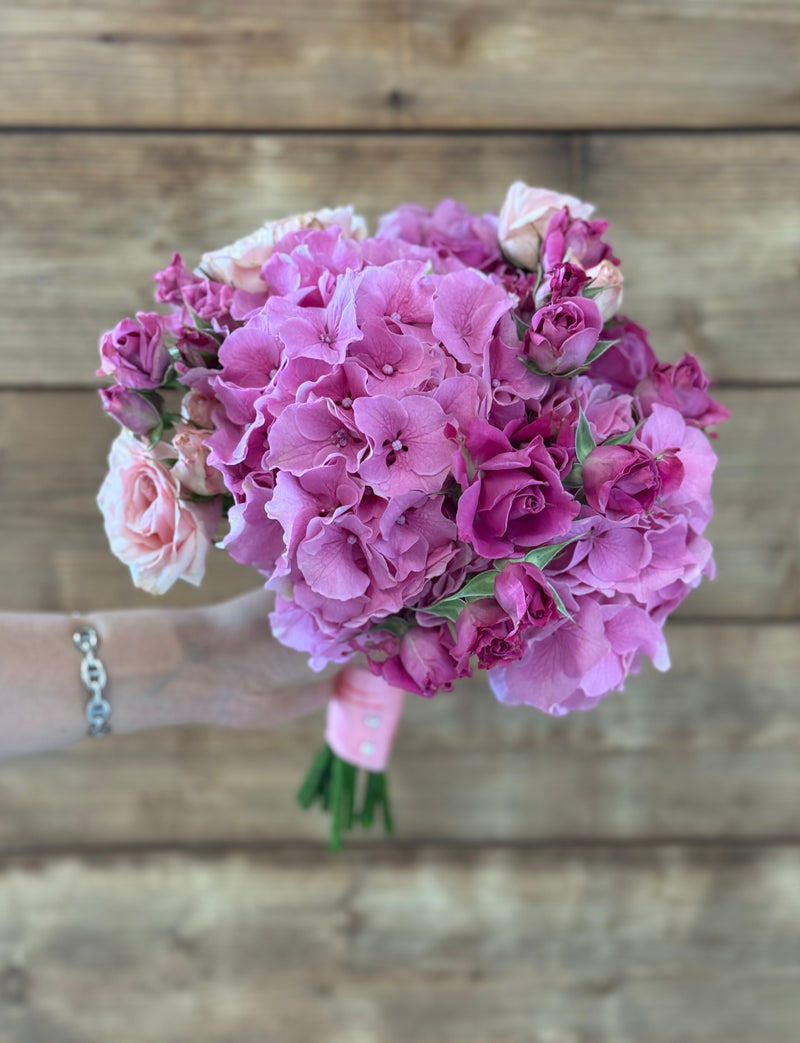 Bridal bouquet shaped with pink hydrangeas and mini roses, delicately tied with a pink ribbon – wedding floral arrangement.