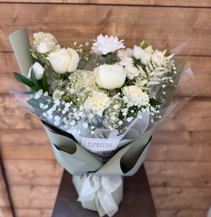 All-white mixed flower bouquet wrapped in light creamy green paper with white ribbon – elegant floral gift arrangement.