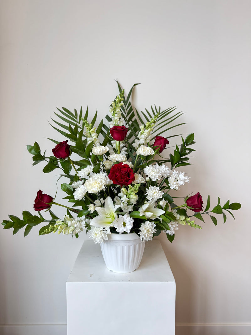 Elegant funeral floral arrangement with white and red blooms in a white vase – sympathy and memorial flowers.
