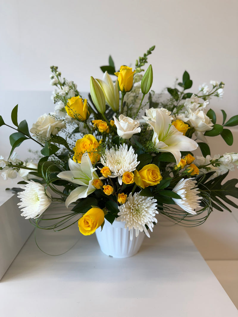 Arrangement of yellow and white flowers in a white vase.