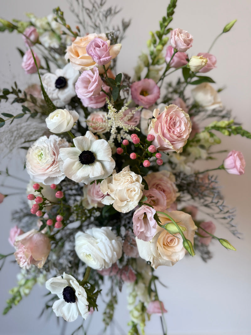 Standing funeral spray with soft pink and white blooms accented with greenery – sympathy and memorial flowers.