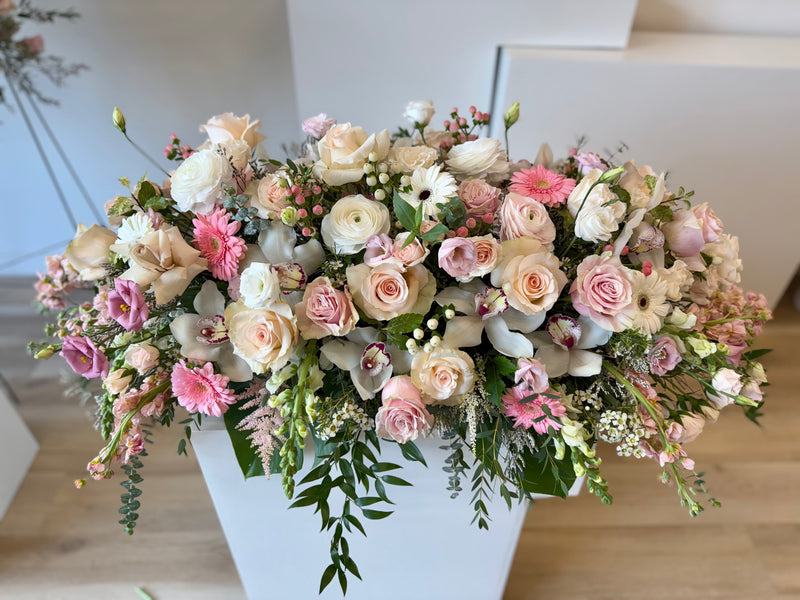 Premium casket floral arrangement with pink and white orchids, ranunculus and roses accented with greenery – funeral and sympathy flowers