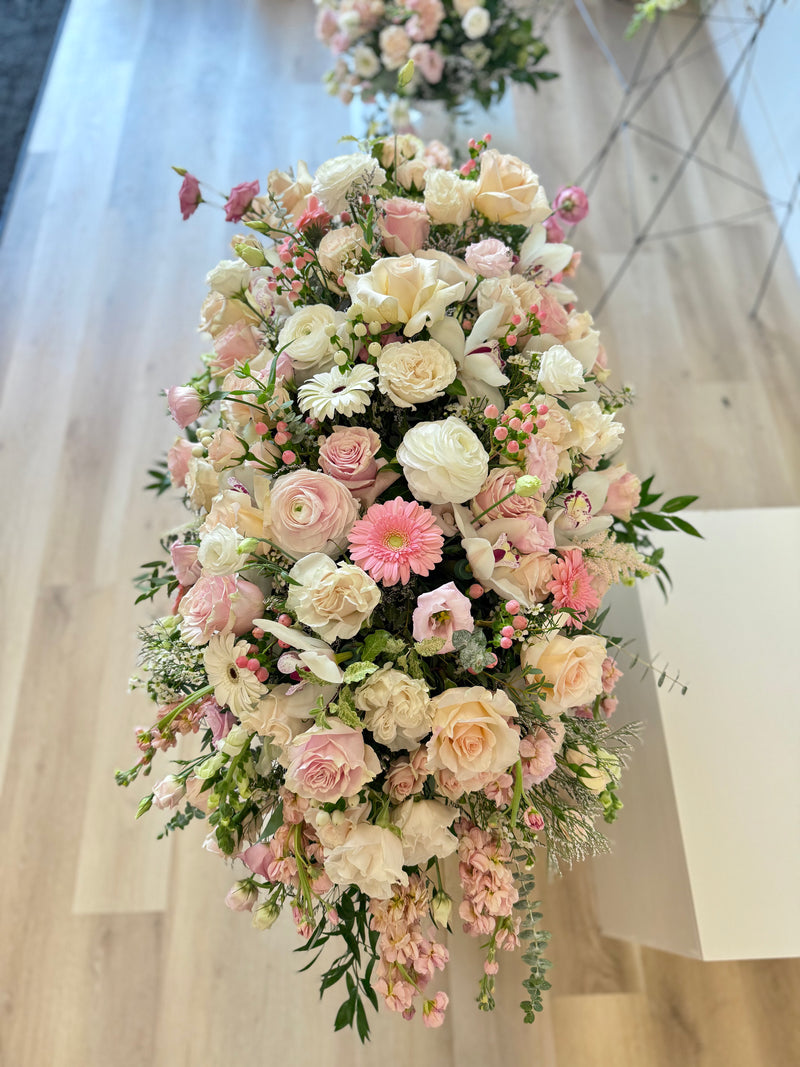 Premium casket floral arrangement with pink and white orchids and ranunculus, accented with greenery – funeral and sympathy flowers.