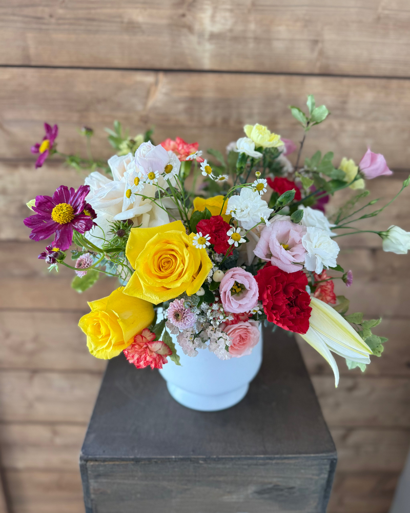 Colourful centrepiece with pink, yellow, red, and purple flowers in a white vase – perfect for home decor or events.