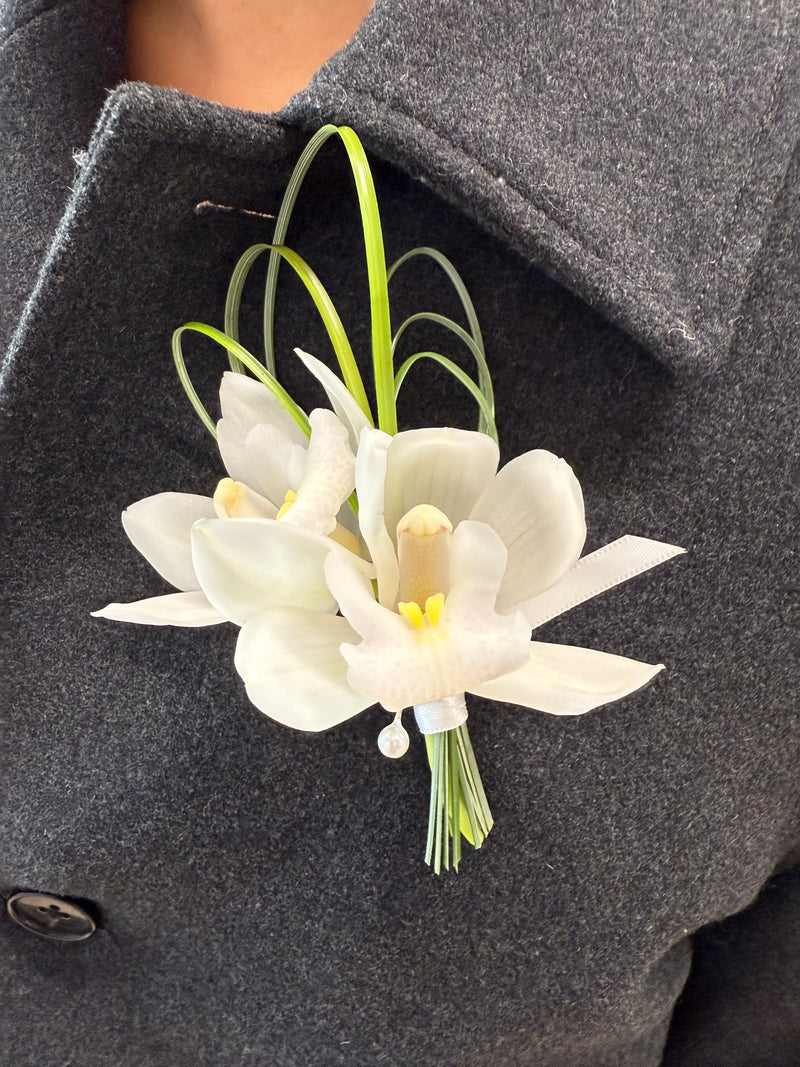 White orchid boutonniere with delicate greenery – wedding and formal event floral accessory.