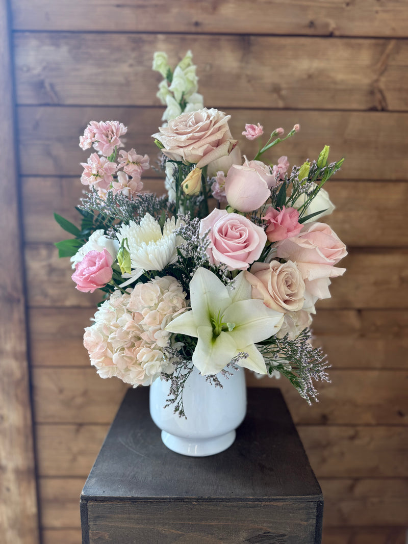 Centrepiece with soft pink blooms paired with pure white flowers in a white vase.