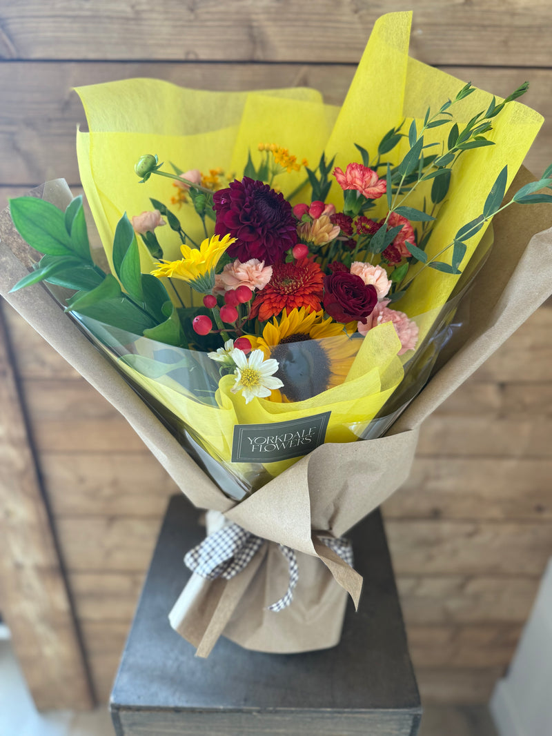 Deep burgundy, bright orange, and golden yellow blooms wrapped in yellow paper with a brown paper sleeve.