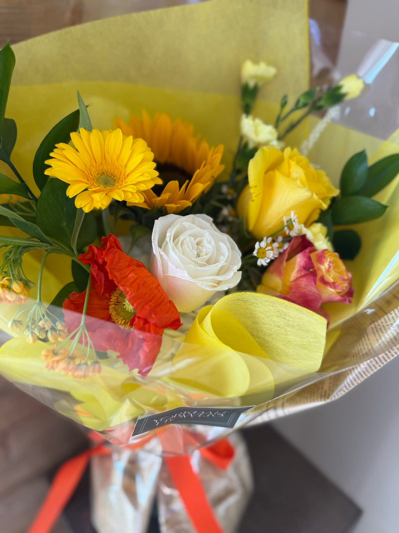 Bright yellow, orange, and white flower bouquet wrapped in newspaper and yellow paper with orange ribbon – perfect for celebrations.